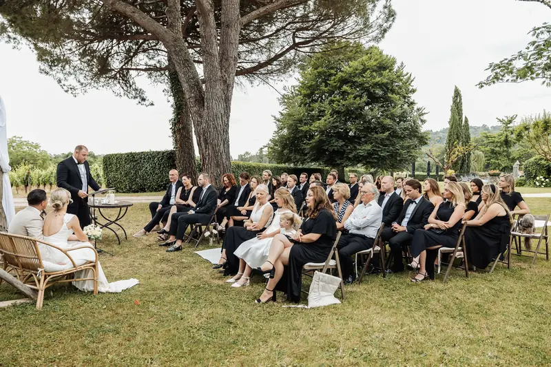 Buitenceremonie onder een grote boom, omringd door gasten