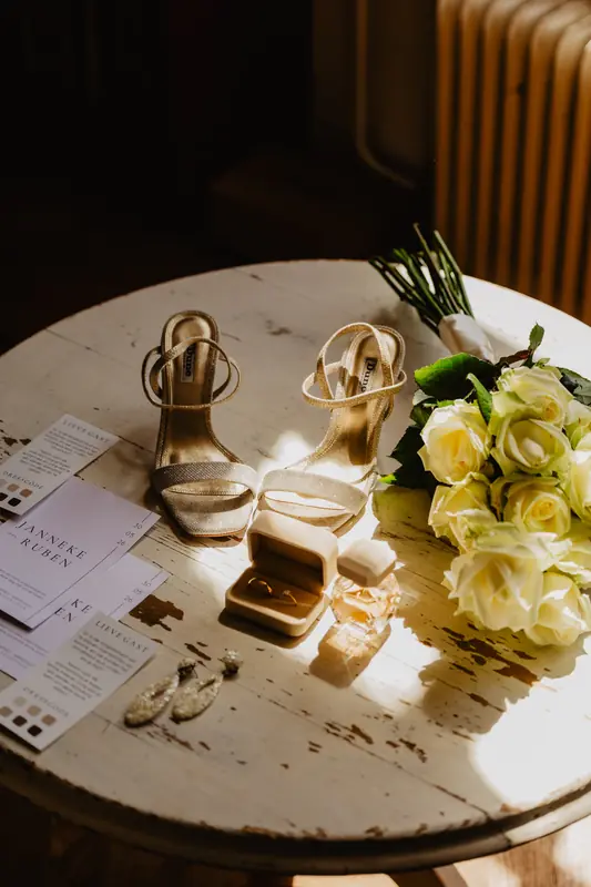 Trouwschoenen, ringen en witte rozen op een tafel
