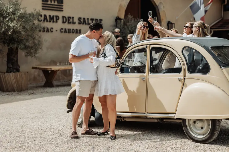 Bruidspaar kust bij een vintage auto terwijl vrienden proosten