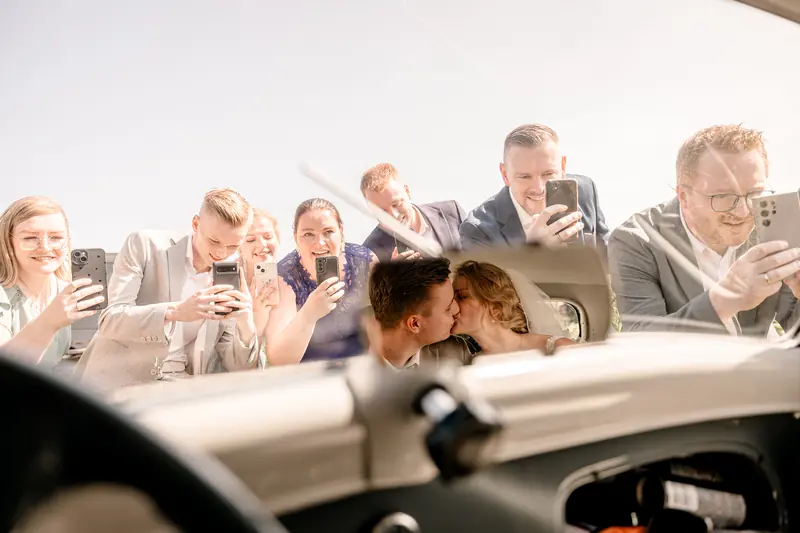 Gasten filmen het bruidspaar dat kust in de auto