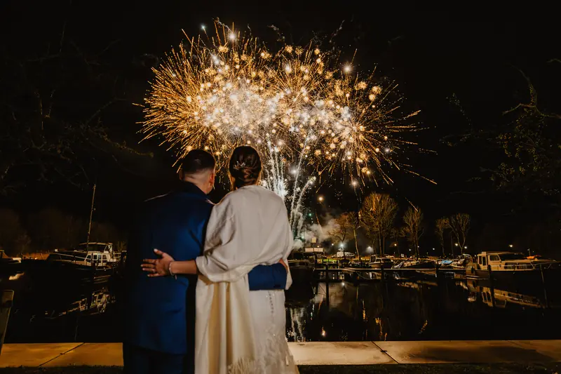 Bruidspaar kijkt naar vuurwerk boven het water