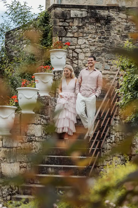 Bruidspaar in roze jurk en linnen pak op een stenen trap vol bloemen