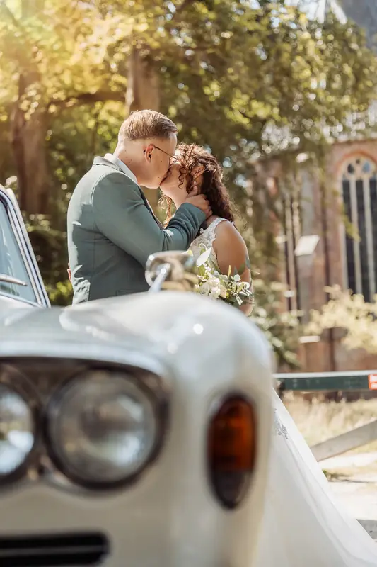 Bruidspaar kust bij een witte oldtimer