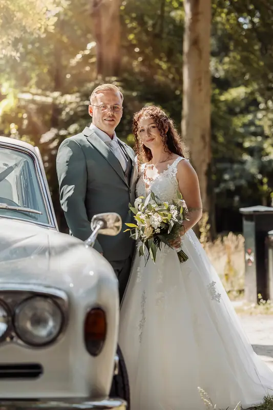 Bruidspaar poseert bij een witte oldtimer