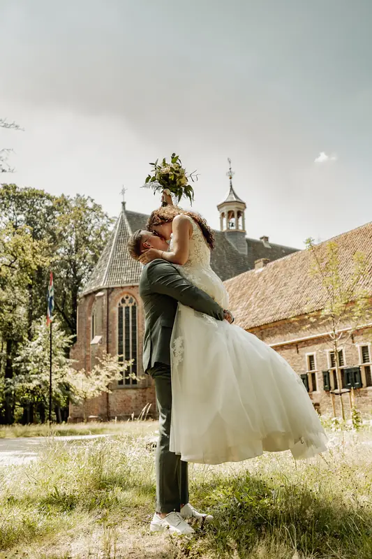 Bruidegom tilt de bruid op bij een kerk